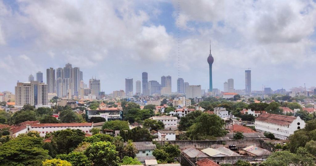 一個晴朗的天空下,可倫坡市中心的高樓大廈與特色建築映照在蔥鬱的綠樹背景中,展現了斯里蘭卡首都的現代都市氛圍。