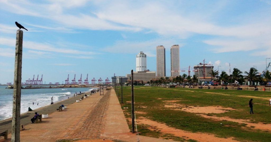 圖片展示了斯里蘭卡可倫坡著名的Galle Face Green海濱公園,公園綠地與遠處的高樓和港口構成了寬闊的景觀,遊客可以在海邊漫步,享受陽光與海風的舒適氛圍。