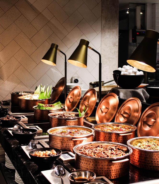 此圖片展示了Courtyard by Marriott Colombo豪華飯店的自助餐區，整齊排列的銅製容器中盛滿了各種美食。黑色石材檯面和金色燈具使整個自助區看起來非常高級且富有現代感。