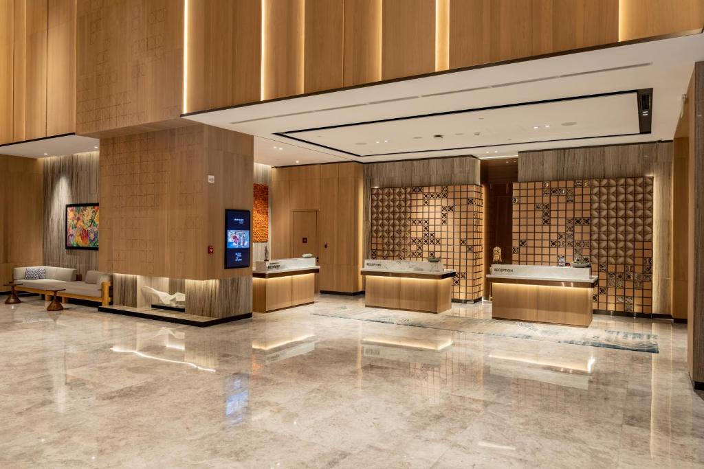此圖片展示了Courtyard by Marriott Colombo的現代化豪華飯店大廳，設計簡約高雅，牆面與接待櫃台運用木質材質，搭配間接照明，營造出舒適且典雅的氛圍。櫃台旁的藝術畫作和休息區的沙發，使空間更具品味。