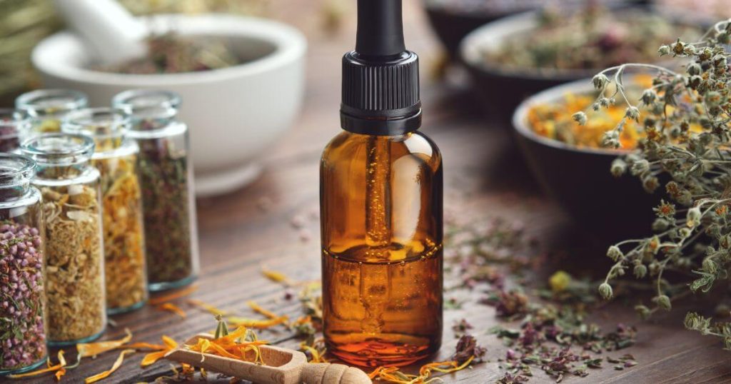 一瓶草本精油置於桌上，周圍環繞著乾燥的花朵與草藥，體現天然草本療法的魅力。