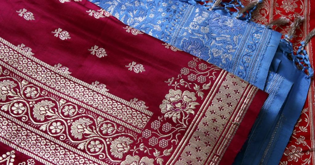 紅色與藍色的精美布料，搭配著金色花卉和幾何圖案，代表傳統紗麗手工織品的優雅風采。